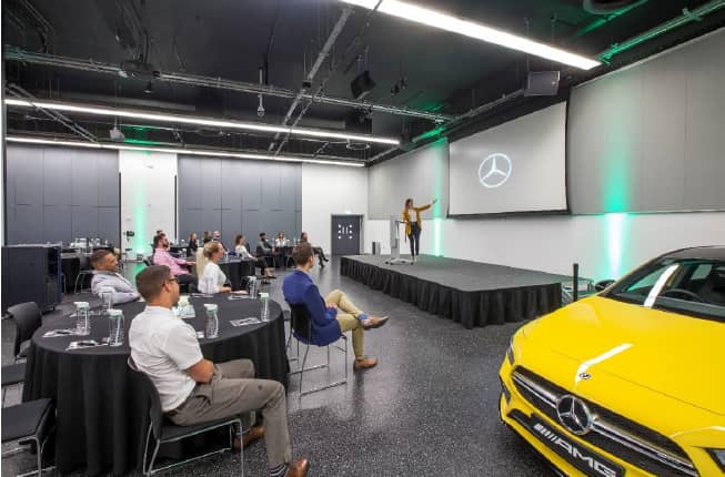 Brooklands Hall event space with stage, round tables, and luxury Mercedes for corporate presentations.