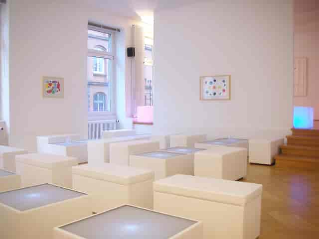 Minimalist gallery breakout room with illuminated seating cubes for networking and art events.