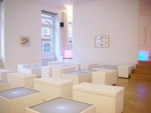 Minimalist gallery breakout room with illuminated seating cubes for networking and art events.