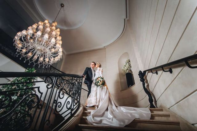 Luxury bridal staircase with ornate ironwork and chandelier for high-end wedding event venue.