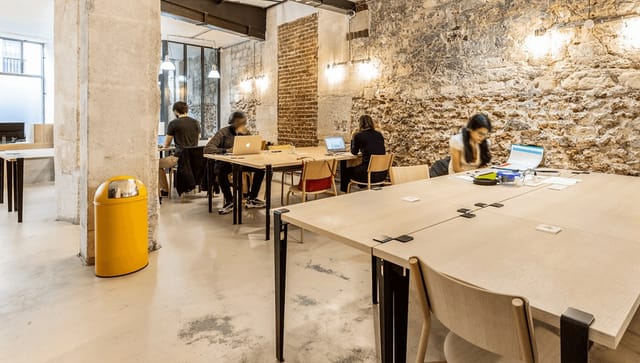 Industrial-chic co-working space with exposed brick, ideal for meetings and collaborative workspaces.