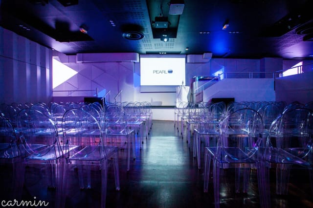 Modern Elyseum banquet hall with tiered seating and ghost chairs for corporate event presentations.