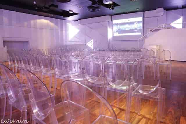 Modern theater-style banquet hall with ghost chairs for corporate presentations and conferences.