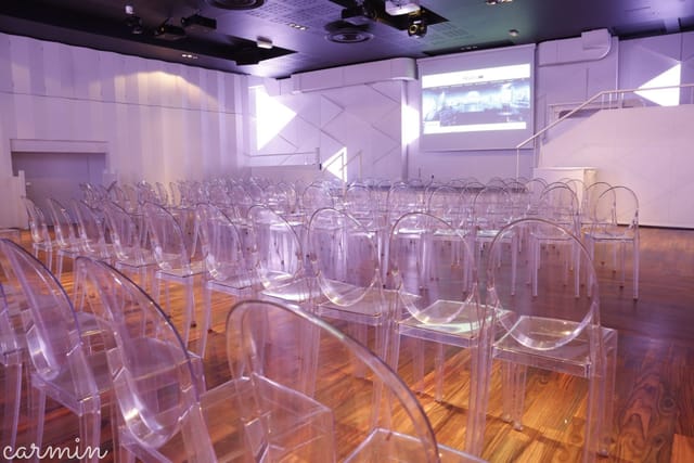 Modern theater-style banquet hall with ghost chairs for corporate presentations and conferences.