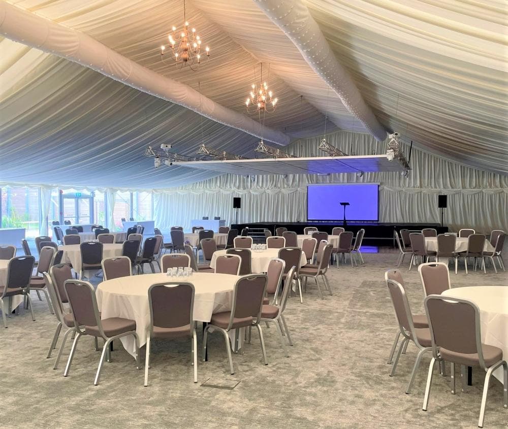 Turner Pavilion marquee set for a corporate conference with stage and cabaret-style seating. - Banner