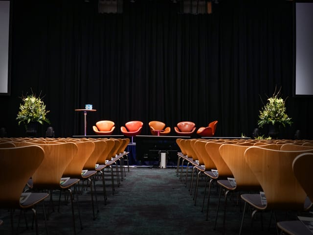 Theater-style meeting room with iconic chairs for corporate panel discussions or keynote events.