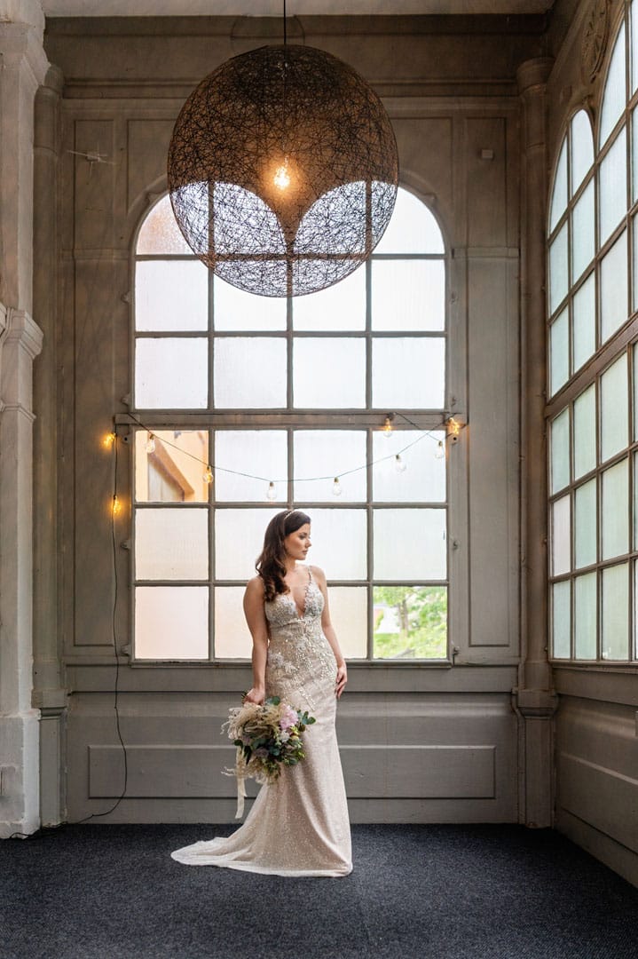 Bride in Glasverandan banquet hall with string lighting for industrial wedding venue photography.