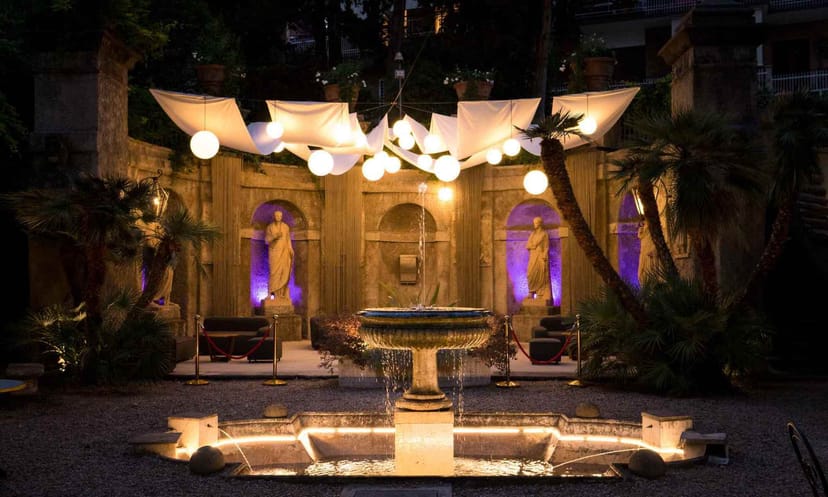 Villa Brasini fountain courtyard: luxury evening event setup with elegant lighting and draping.