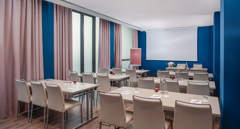 Classroom-style meeting room at NH Hotel Rome with AV screen for corporate events and workshops.