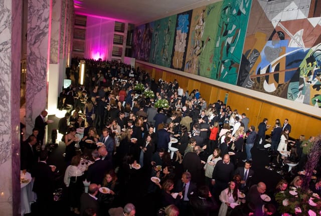 Networking reception in historic Palazzo dei Congressi foyer with large-scale art.