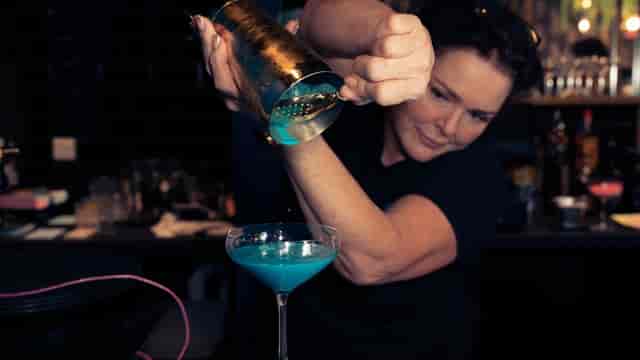 Bartender crafting vibrant cocktail at Serendipity bar, ideal for evening reception event styling.