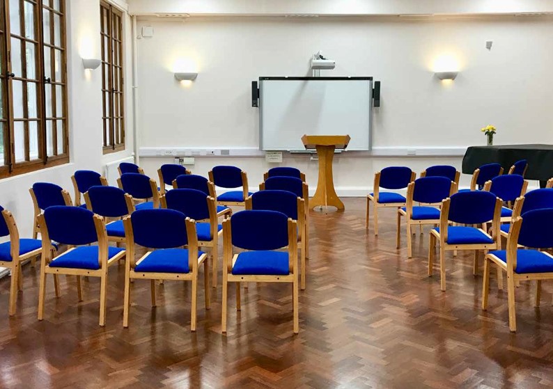 Lecture room with blue chairs, podium, and screen for meetings and workshops.