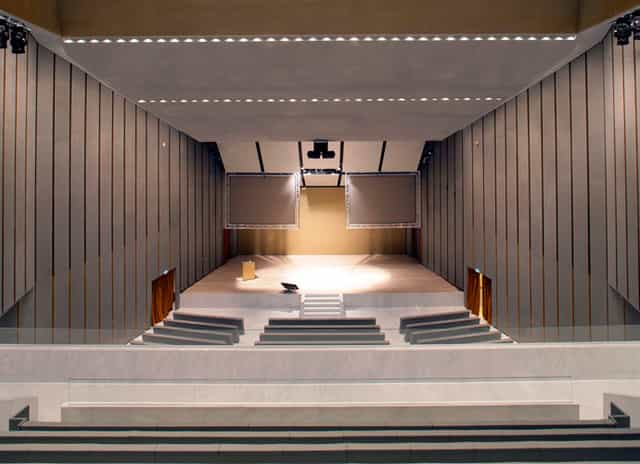 Modern Aula Magna auditorium with dual screens for corporate keynotes and professional events.