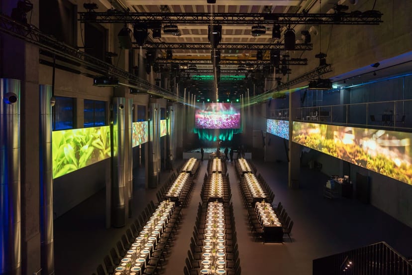 Industrial-chic JED Events hall set for gala dinner with LED displays and banquet seating.