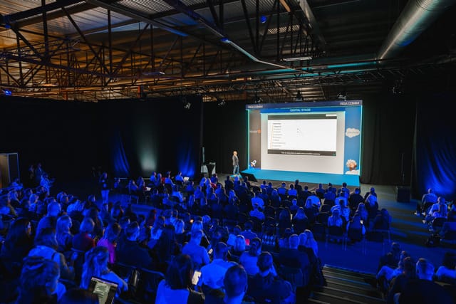 Corporate keynote presentation in a warehouse venue with mood lighting and large screen.