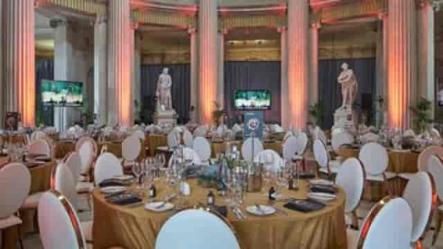 Gala dinner in neoclassical City Hall with gold linens and pillars, elegant event venue.
