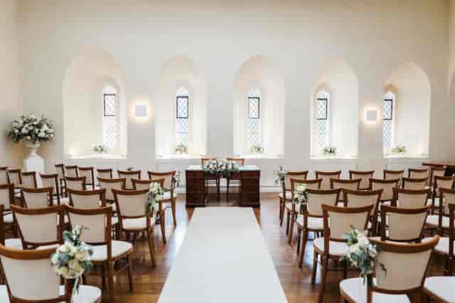 Minimalist wedding ceremony in Farnham Castle chapel with arched windows and floral aisle decor.