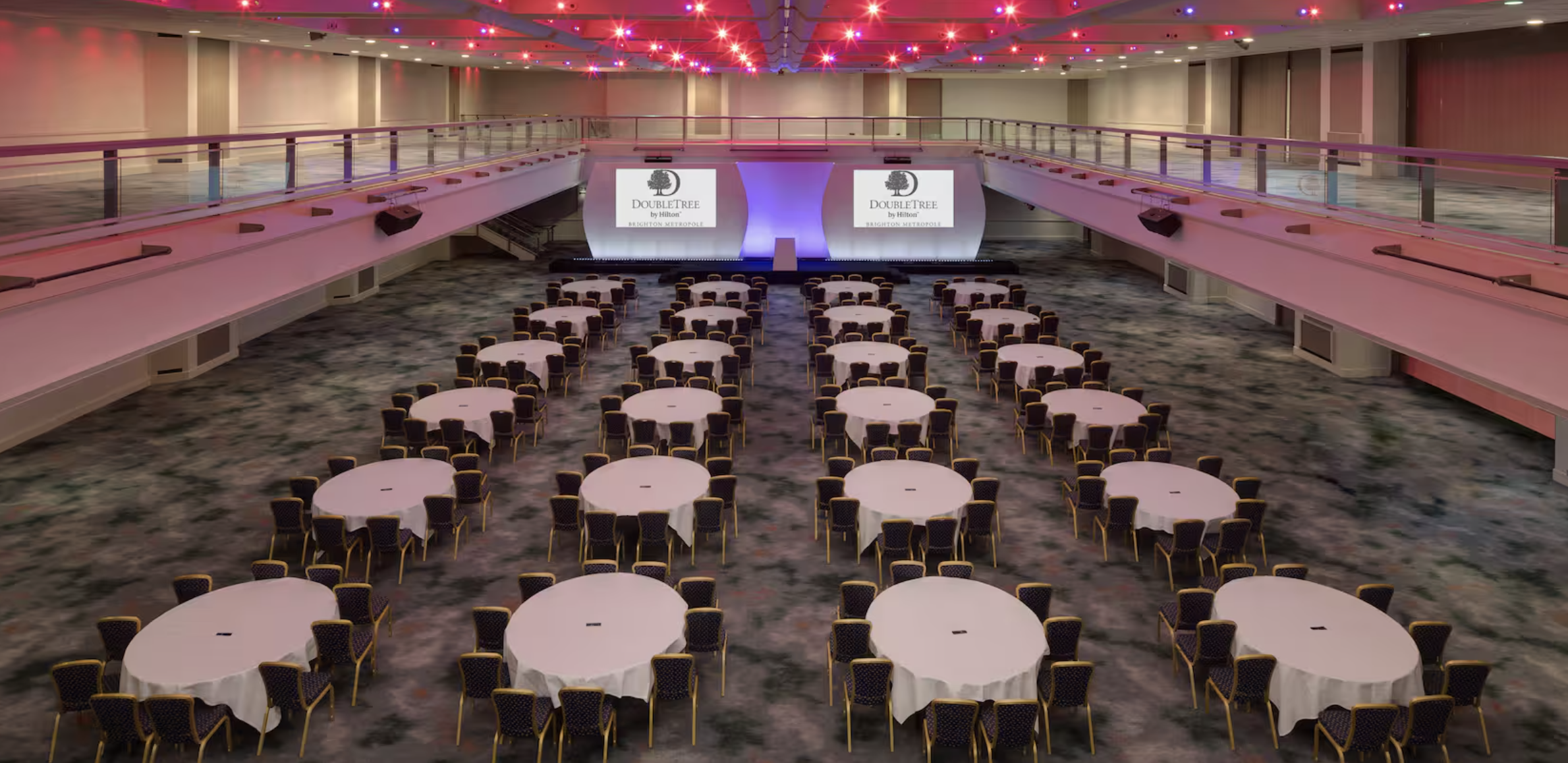 Spacious conference venue at DoubleTree Brighton with round tables and dynamic lighting. - Banner