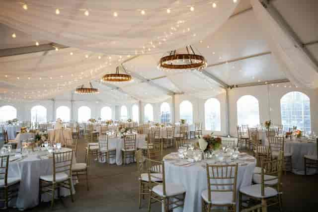 Clear-span tent wedding at EY Lobby with bistro lighting and cross-back chairs.