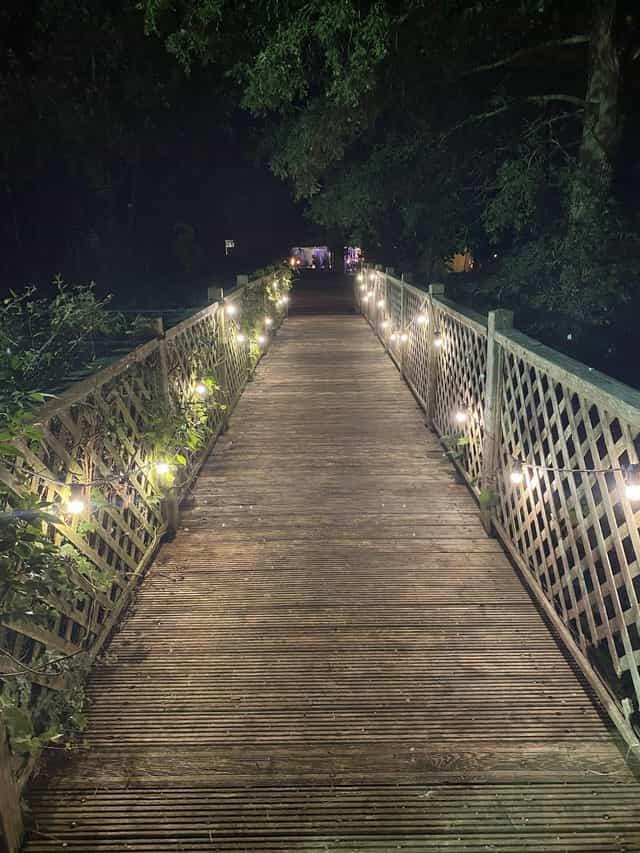 Glamping site rustic bridge with ambient festoon lighting for evening wedding or event venue.
