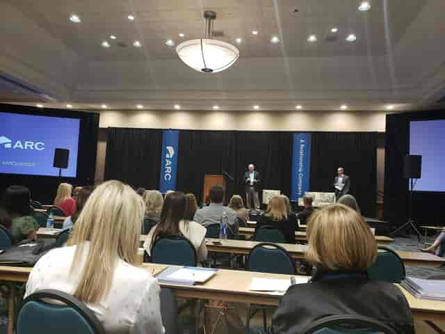 Classroom-style corporate plenary session with stage banners at BJCC for professional events.