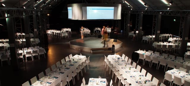 Industrial corporate banquet hall with central stage for gala dinners and event presentations.