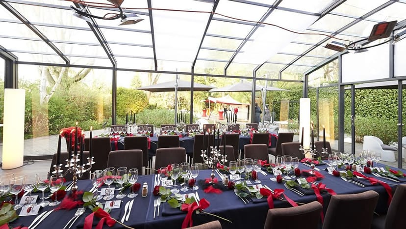 Elegant greenhouse banquet hall with red floral decor for wedding or gala dinner.
