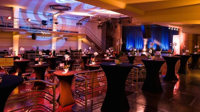 Albert Hall Brussels cocktail reception: industrial event space with stage and high-top tables.