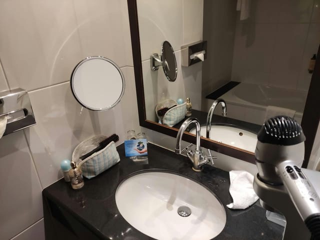 Jacques Tati I hotel bathroom with cluttered vanity, ideal for event planning and venue reviews.