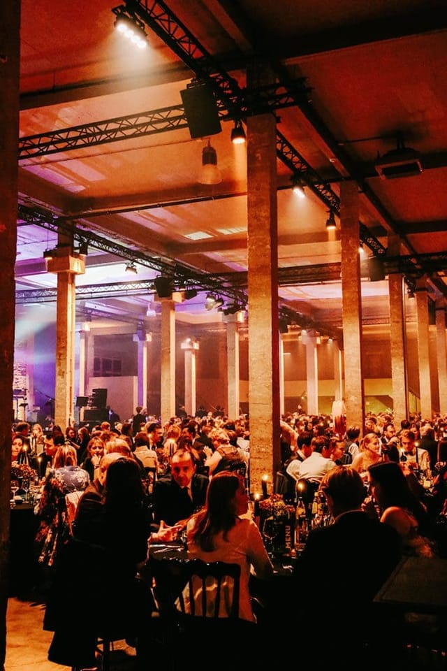 Gala dinner in industrial-chic venue with architectural columns, elegant corporate event lighting.
