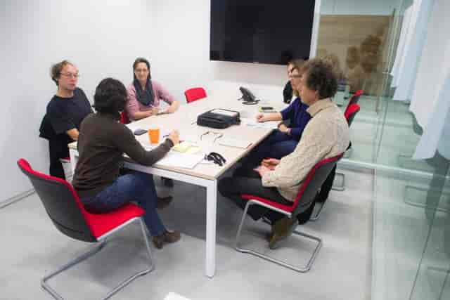 Small-group breakout session in a cramped, utilitarian Eco-Dynamic workspace for corporate meetings.