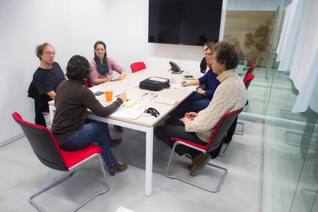 Small-group breakout session in a cramped, utilitarian Eco-Dynamic workspace for corporate meetings.