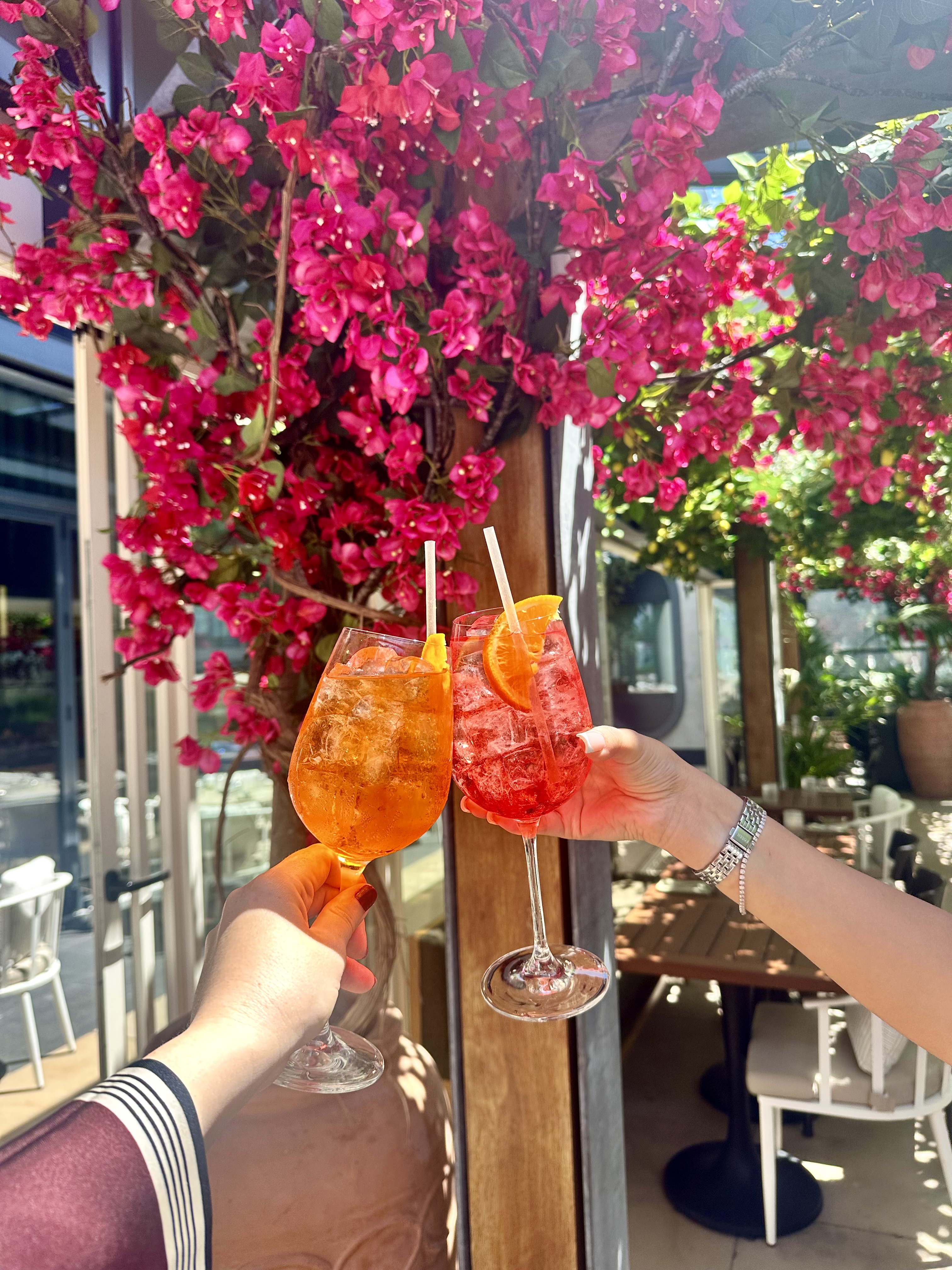 Vibrant outdoor terrace at HERA Restaurant with colorful cocktails and bougainvillea.