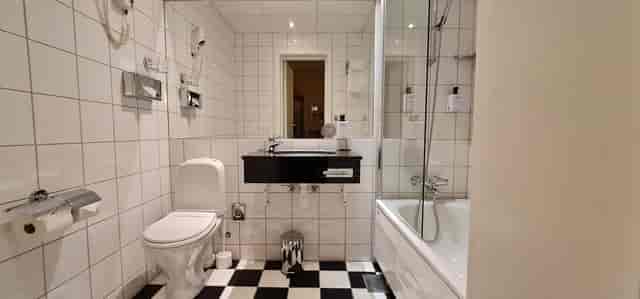 Dated hotel bathroom at Scandic Holberg: checkerboard floors for corporate event planning.
