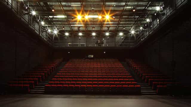 Industrial black-box theater with tiered seating for corporate keynotes and product launches.
