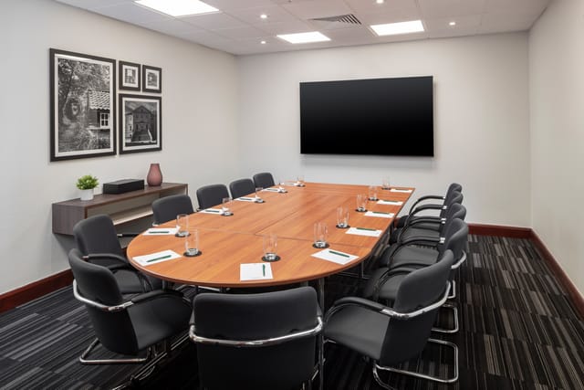 Meeting room at Holiday Inn London-Bexley, featuring an oval table and presentation screen.