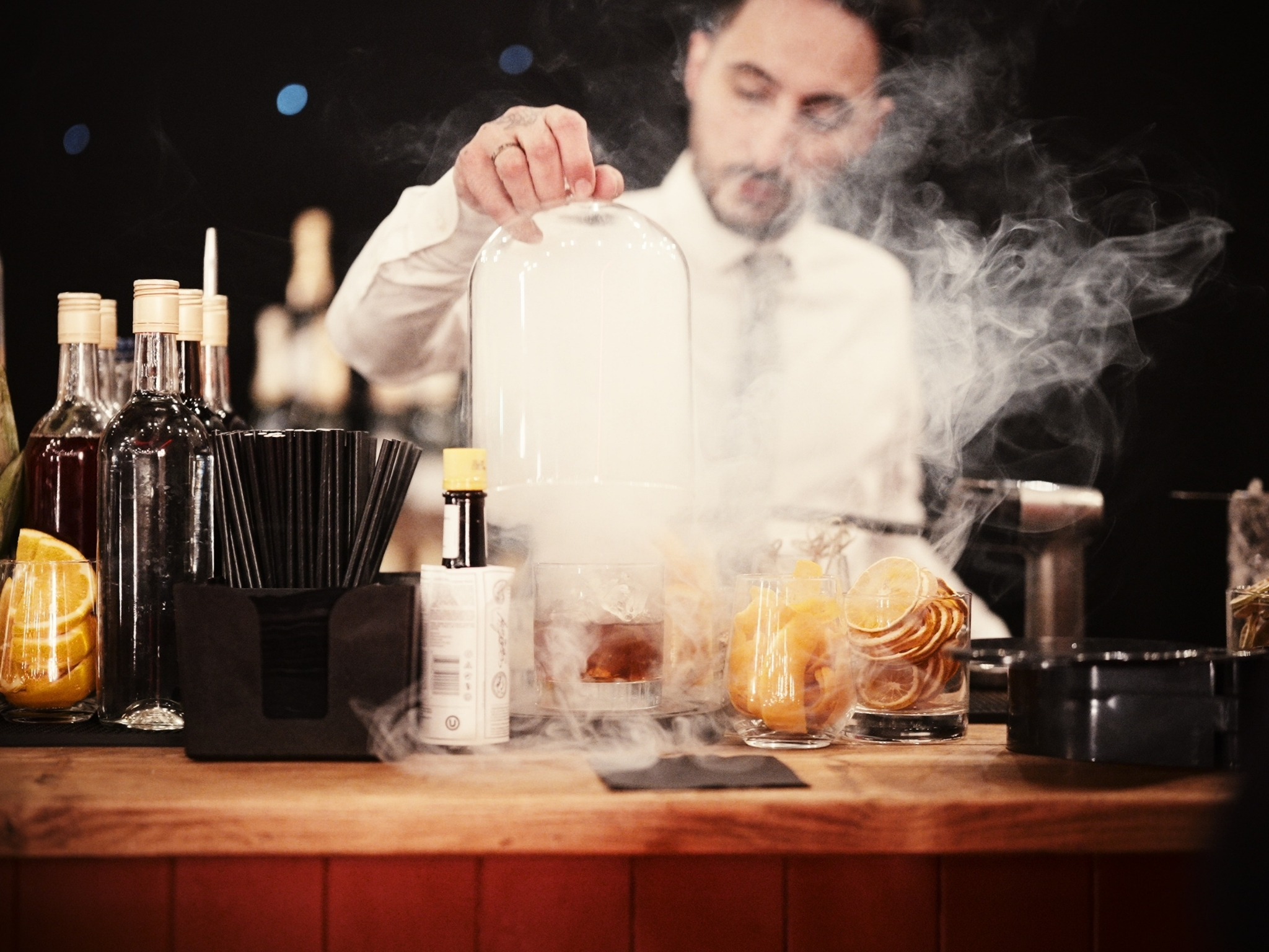 Stylish bartender creating a cocktail with smoke at The Magicians Table event venue. - Banner