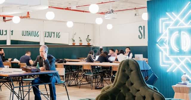 Modern coworking meeting room with communal tables for networking and breakout sessions.