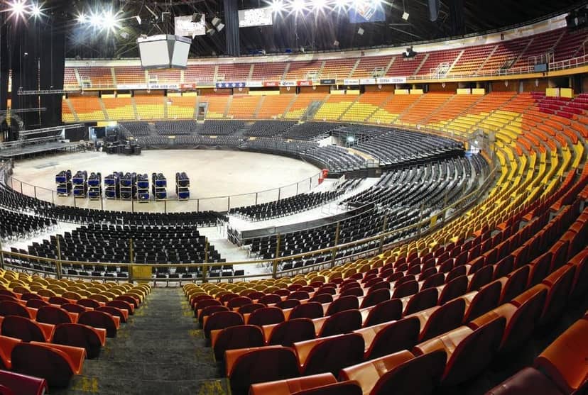 Palacio de los Deportes arena interior during event load-in, featuring tiered seating and stage setup.