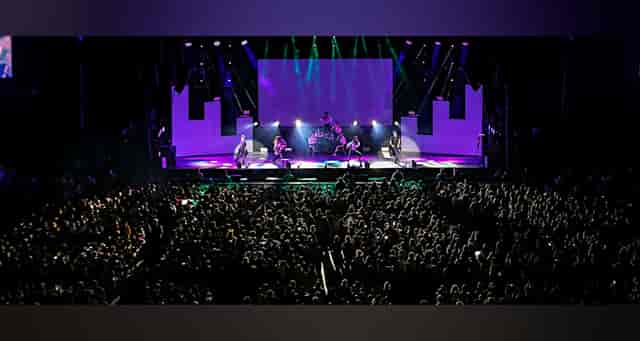 Palacio de los Deportes arena plenary session with stage lighting and screen for corporate events.