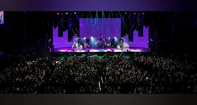 Palacio de los Deportes arena plenary session with stage lighting and screen for corporate events.