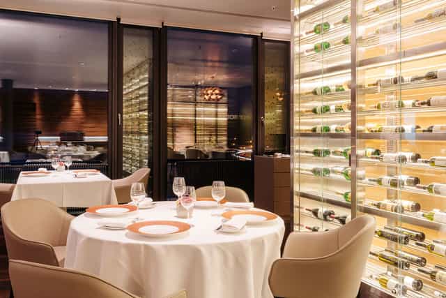 Upscale private dining room with illuminated wine cellar for corporate events and VIP dinners.