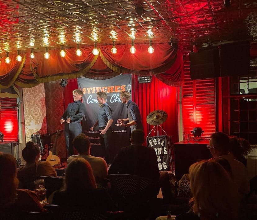 In Stitches comedy club showcase with intimate red decor and warm lighting.