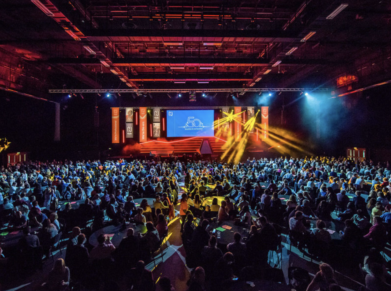 Brighton Centre venue with vibrant lighting and packed audience at a large event. - Banner