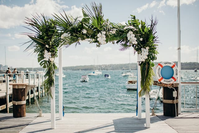 Outdoor wedding setup with floral arch overlooking waterfront at Vaucluse Yacht Club.