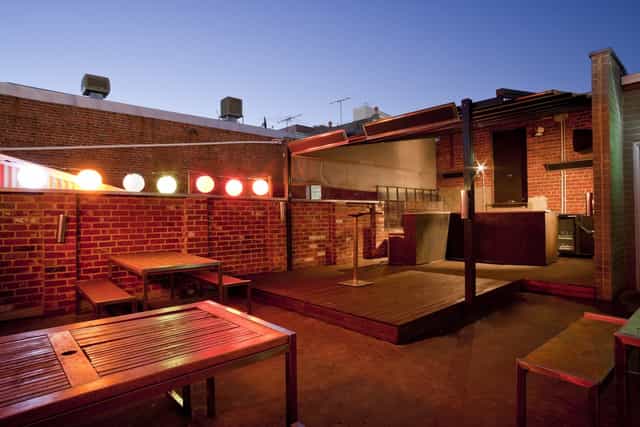 Industrial-chic outdoor venue with stage and string lighting for networking events and mixers.