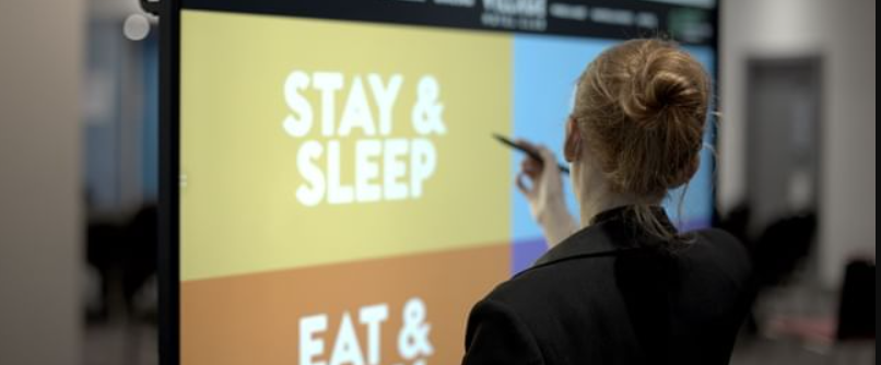 Engaged attendee at Village Hotel Reading's Inspiration Suite conference, vibrant digital screens. - Banner