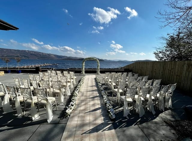 Outdoor wedding venue, Glen Luss Suite, with white chairs and elegant archway by Loch Lomond.