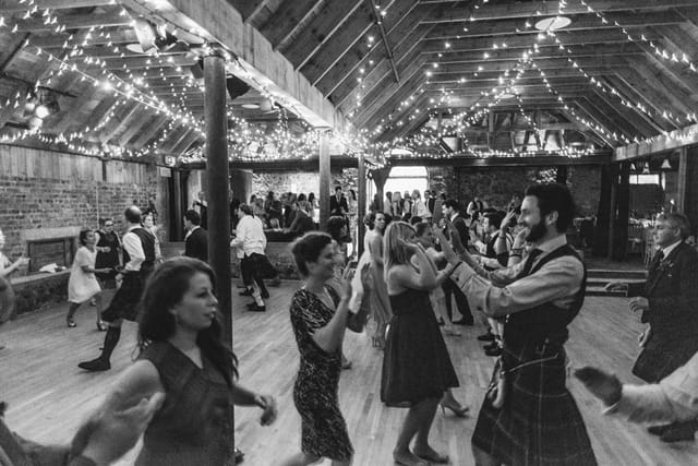 Vibrant wedding celebration at The Byre, featuring guests dancing under fairy lights.