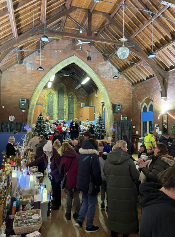 Festive holiday market at Great Preston Village Hall with crowded stalls and performance stage.